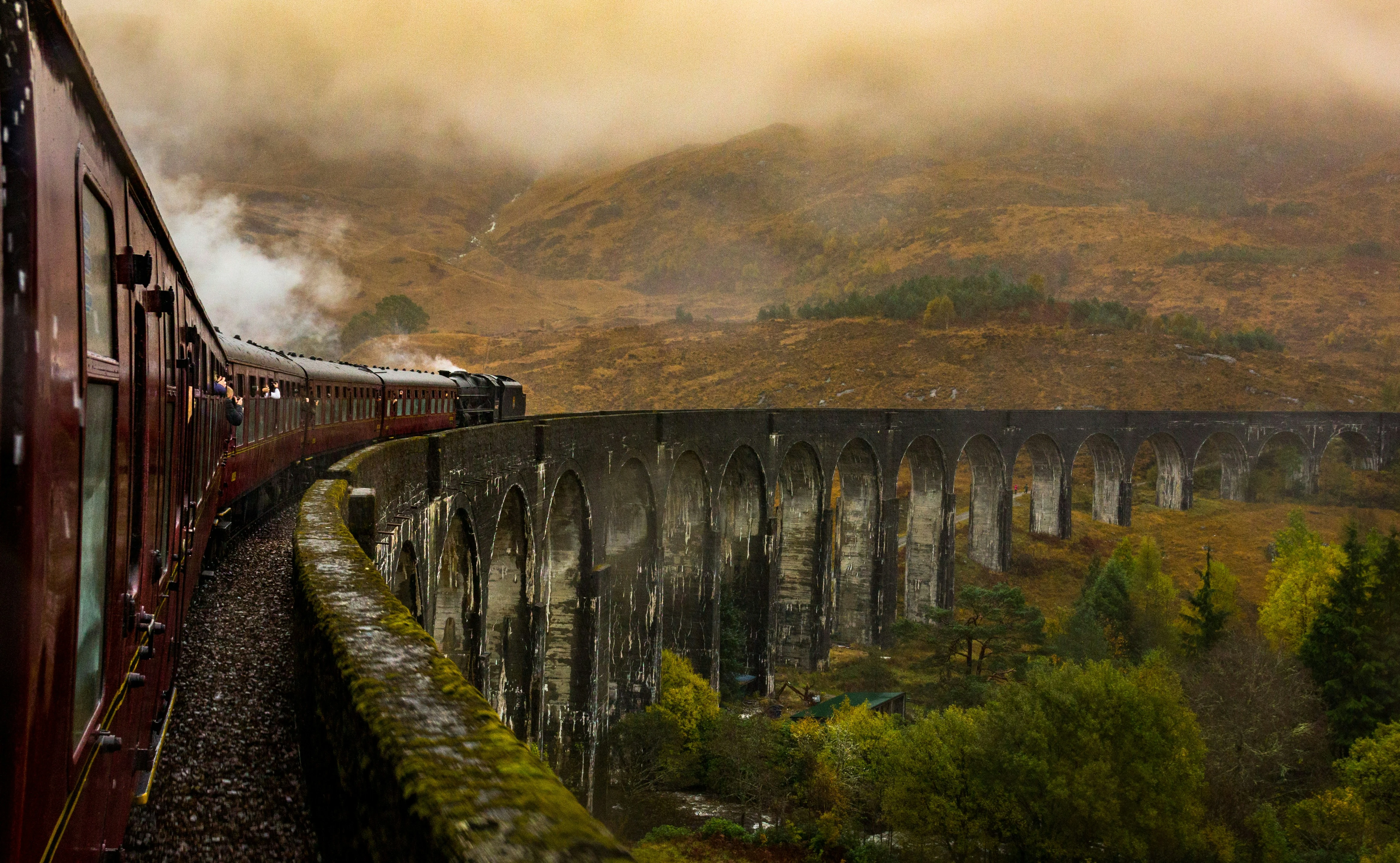 Historic luxury train crossing a grand stone viaduct surrounded by misty mountains