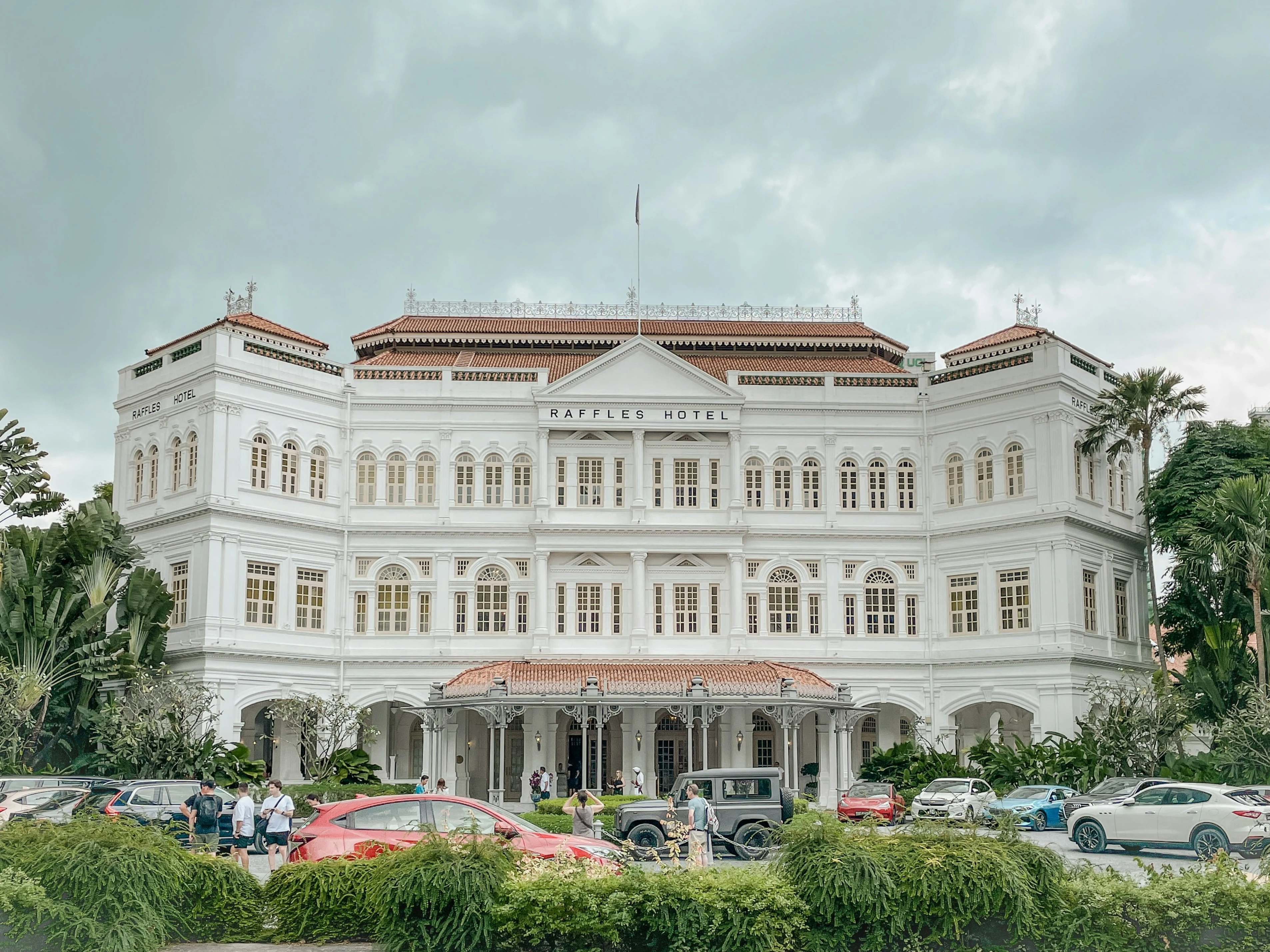 Grand historic white facade of Raffles Hotel Singapore surrounded by tropical palms and lush greenery